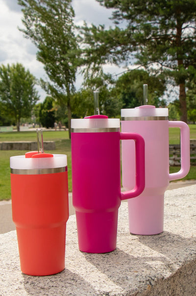 Drei Stanley Becher in Pink und Orange mit HALM Glasstrohhalmen. Diese wiederverwendbaren Glasstrohhalme sind die perfekte nachhaltige Ergänzung für große Trinkbecher.
