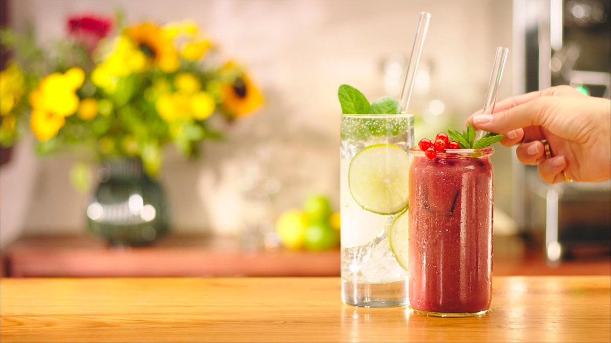 Wiederverwendbare HALM Glasstrohhalme im Einsatz für verschiedene Getränke wie Smoothie und Gin Tonic auf einem Banner präsentiert.