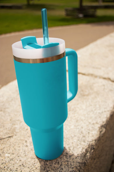 Wiederverwendbare HALM Glasstrohhalme in hellblau in einem Stanley Cup Quencher Trinkbecher als Mood-Foto im Freien.