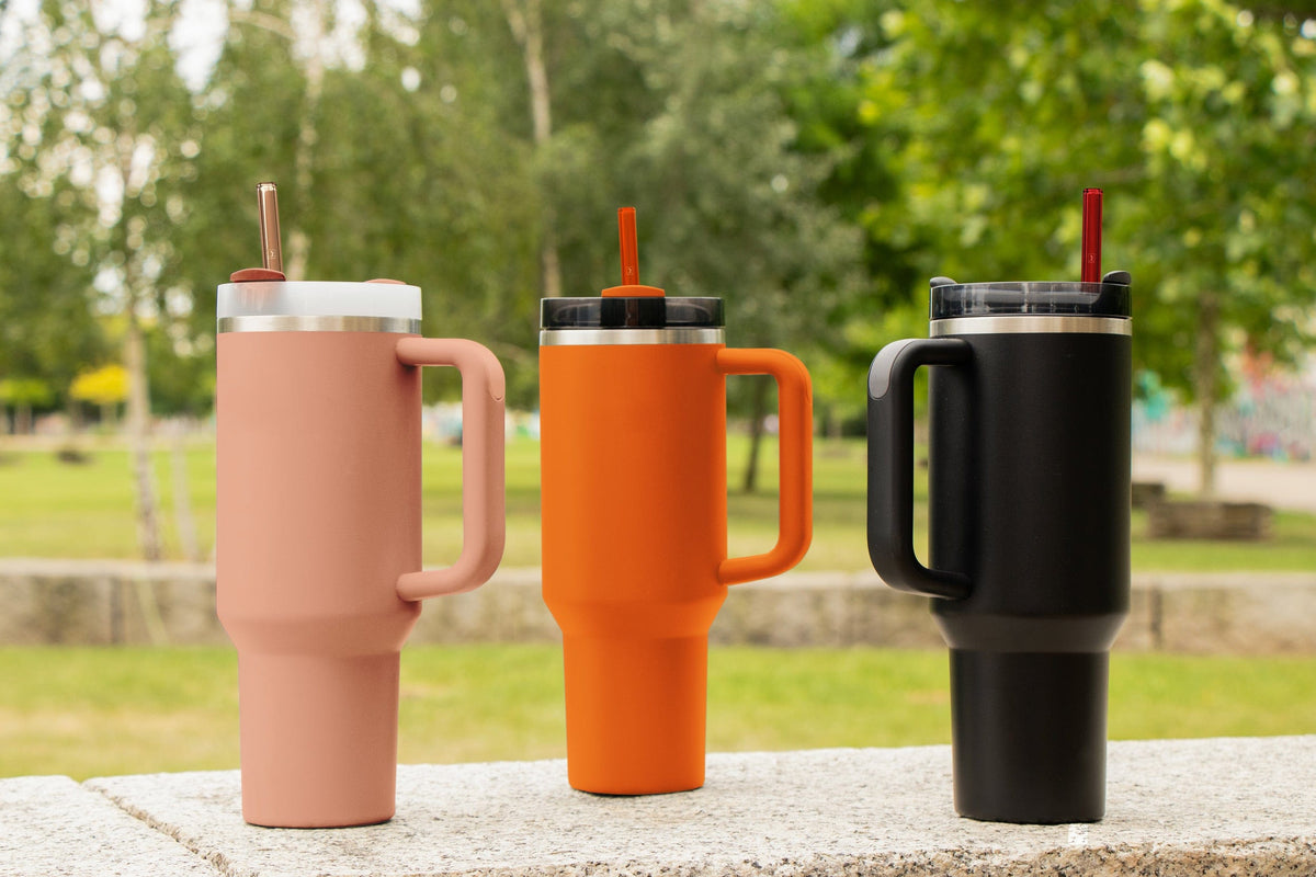 Wiederverwendbare HALM Glasstrohhalme in Pink, Orange und Rot für den Stanley Cup Quencher Trinkbecher auf einem farblich passenden Untergrund.